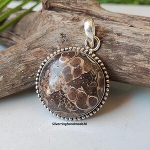 May include: A round pendant with a brown and white agate stone set in a silver bezel. The pendant has a beaded edge and a silver bail.