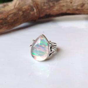 Puede incluir: Un anillo de plata con una opala en forma de lágrima. La opala es iridiscente con tonos de rosa, verde y azul.