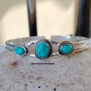 以下が含まれることがあります： シルバー製のバングルブレスレット。ターコイズの石が3つ、シルバーのベゼルにセットされています。ブレスレットはオープンタイプで、サイズ調整が可能です。