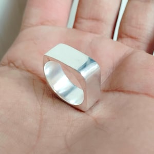 May include: A silver square shaped ring with a smooth, polished finish.