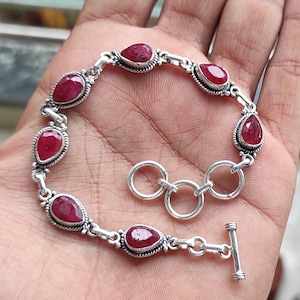 May include: A silver bracelet with red ruby gemstones. The bracelet has a lobster clasp closure.