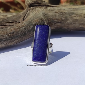 以下が含まれることがあります： 長方形のラピスラズリをセットしたシルバーリング。石は深い青色で白い筋が入っています。