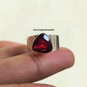 May include: A silver ring with a triangular red gemstone. The ring is wide and has a flat band.