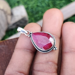 May include: A teardrop-shaped pendant with a red ruby gemstone set in sterling silver. The pendant has a delicate silver bail for attaching to a chain.