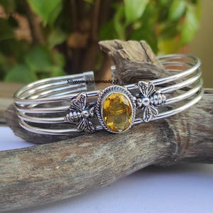 Op de afbeelding: Zilveren manchetarmband met een ovale, gele edelsteen en bijenmotieven. De armband heeft vier parallelle banden en ligt op hout. De tekst "Silverringhandmade20" is zichtbaar.
