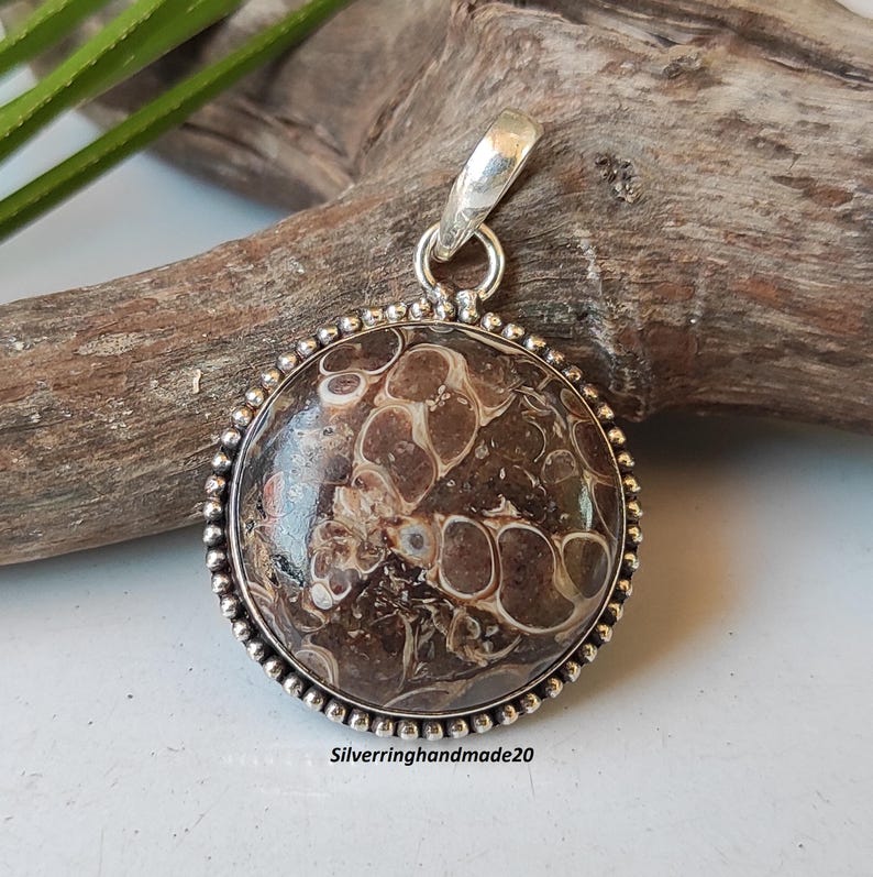 May include: A round brown and white agate pendant with a silver bezel and bail. The pendant is approximately 1 inch in diameter.