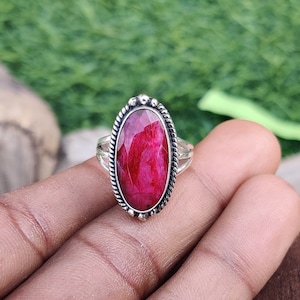 May include: A silver ring with a large oval-shaped ruby gemstone. The ruby is a deep red color and has a faceted cut.