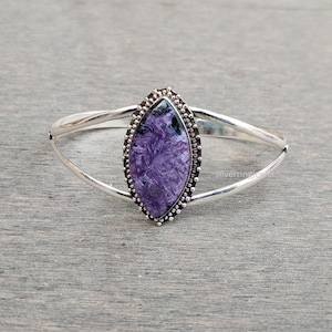 Pode incluir: Um bracelete de prata com uma pedra roxa e preta engastada em um bezel de prata. A pedra tem um padrão de mármore.