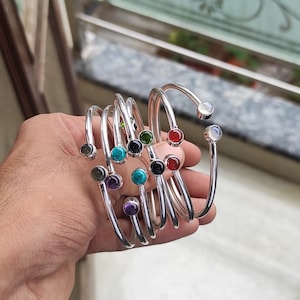 Pode incluir: Um conjunto de pulseiras de prata com pedras preciosas de diferentes cores. As pulseiras estão empilhadas umas sobre as outras e apresentam uma variedade de cores, incluindo turquesa, vermelho, verde e roxo.