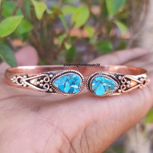 Peut inclure: Un bracelet en cuivre avec deux pierres turquoise serties au centre. Le bracelet est décoré de motifs sur les côtés.