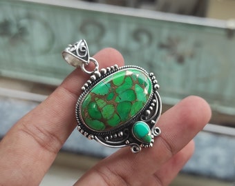 May include: A silver pendant with a green and gold turquoise stone set in a detailed silver frame. The pendant has a smaller turquoise stone hanging from the bottom.
