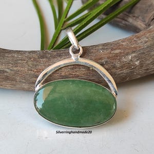 May include: A silver pendant with a green oval gemstone set in a silver frame. The pendant is designed to spin freely.