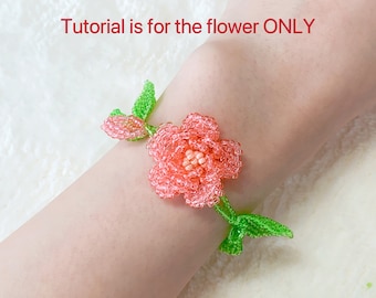 May include: A beaded flower bracelet featuring a central pink blossom with a light peach center, surrounded by small green beaded leaves and a small bud. The text "Tutorial is for the flower ONLY" is printed in red above the floral design.