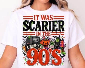 May include: A white t-shirt featuring a graphic print with the text IT WAS SCARIER IN THE 90'S. The design includes a television, a cassette tape labeled GOOD SCARES BETTER TIMES, a jack-o'-lantern, a handheld game console, and a cell phone.