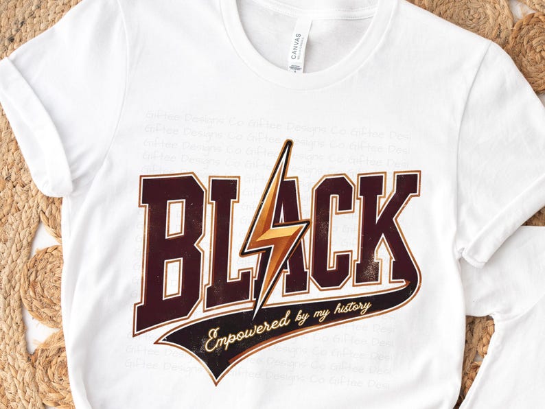 May include: White t-shirt with a graphic print of the word "BLACK" in brown letters with a gold lightning bolt. The text "Empowered by my history" is printed in a curved line below the word "BLACK".