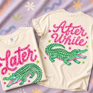 May include: Two cream-colored t-shirts with colorful designs. One shirt features the word "Later" in pink script above a green alligator. The other shirt has "After While" in pink script and a green alligator.