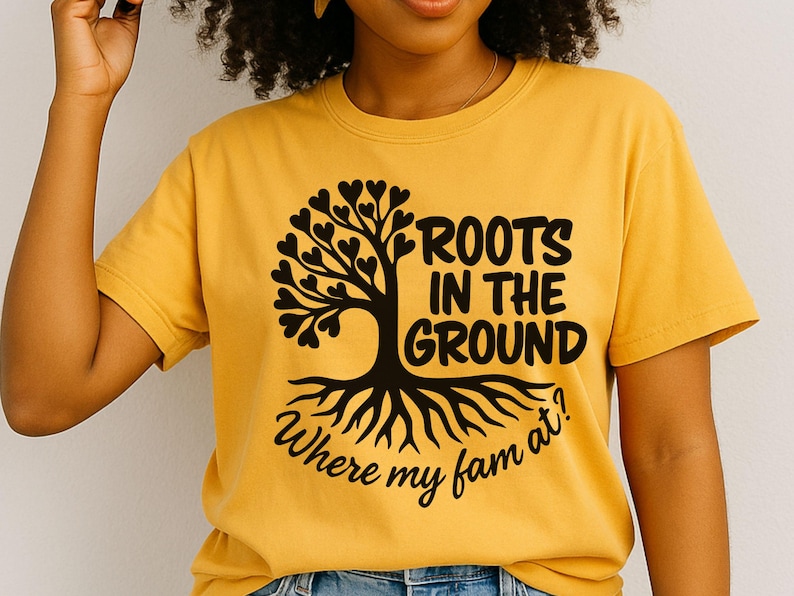 May include: Mustard yellow t-shirt with a black tree graphic. The tree has heart-shaped leaves and the text "ROOTS IN THE GROUND Where my fam at?" in a stylized font. The shirt is a crew neck.