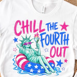 May include: A white t-shirt featuring a graphic of the Statue of Liberty wearing pink sunglasses, lounging in a red, white, and blue star-patterned pool float while holding a martini glass. The text reads CHILL THE FOURTH OUT in pink and blue.