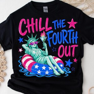 May include: A black t-shirt featuring a graphic of the Statue of Liberty wearing pink sunglasses, lounging in a red, white, and blue striped pool float while holding a martini glass. The text reads CHILL THE FOURTH OUT in pink and blue.