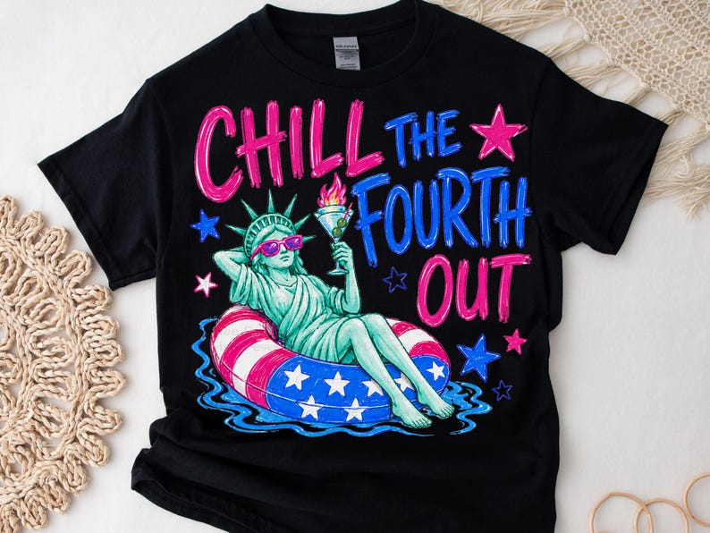 May include: A black t-shirt featuring a graphic of the Statue of Liberty wearing pink sunglasses, lounging in a red, white, and blue striped pool float while holding a martini glass. The text reads CHILL THE FOURTH OUT in pink and blue.