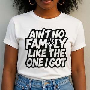 May include: White t-shirt with the text "AIN'T NO FAMILY LIKE THE ONE I GOT" in a black, bold font. The shirt has a crew neck and short sleeves. The text includes a stylized tree graphic.