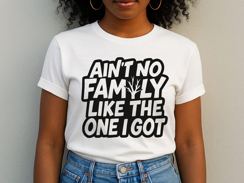 May include: White t-shirt with the text "AIN'T NO FAMILY LIKE THE ONE I GOT" in a black, bold font. The shirt has a crew neck and short sleeves. The text includes a stylized tree graphic.
