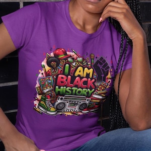 May include: Purple t-shirt with a colorful graphic design featuring a cartoon character, a boombox, and the text "I AM BLACK HISTORY".
