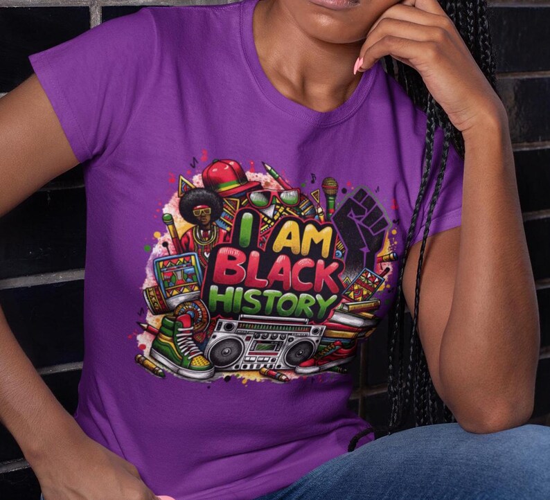 May include: Purple t-shirt with a colorful graphic design featuring a cartoon character, a boombox, and the text "I AM BLACK HISTORY".