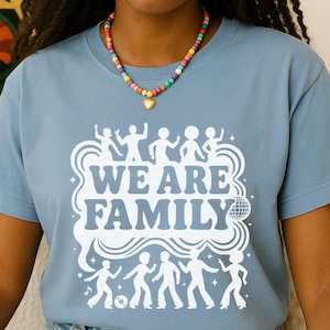 May include: A light blue t-shirt with the words "WE ARE FAMILY" in white, along with dancing figures and a disco ball graphic. The shirt is made of soft material and is suitable for casual wear.