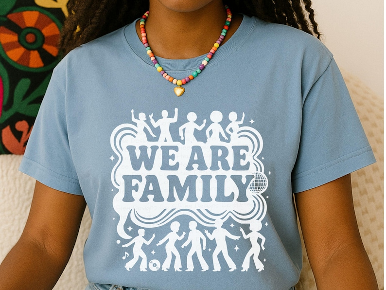 May include: A light blue t-shirt with the words "WE ARE FAMILY" in white, along with dancing figures and a disco ball graphic. The shirt is made of soft material and is suitable for casual wear.