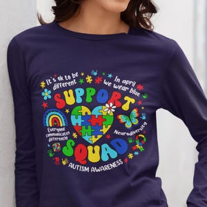 May include: Navy blue long-sleeve shirt with a colorful graphic design featuring a puzzle piece heart, rainbow, butterfly, and the text "Support Squad Autism Awareness".