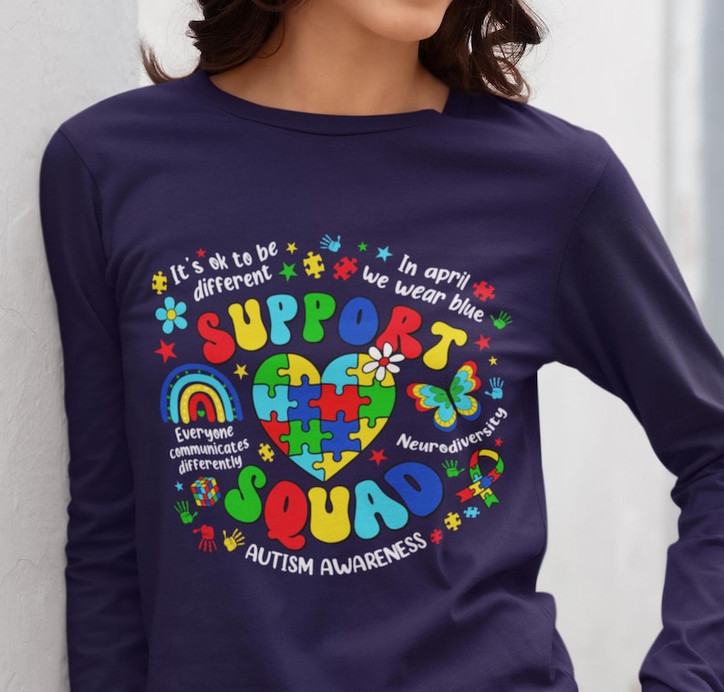 May include: Navy blue long-sleeve shirt with a colorful graphic design featuring a puzzle piece heart, rainbow, butterfly, and the text "Support Squad Autism Awareness".