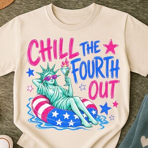 May include: A cream-colored t-shirt featuring a graphic of the Statue of Liberty wearing pink sunglasses, lounging in a red, white, and blue striped pool float while holding a martini. The text reads CHILL THE FOURTH OUT in pink and blue.