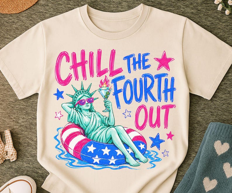 May include: A cream-colored t-shirt featuring a graphic of the Statue of Liberty wearing pink sunglasses, lounging in a red, white, and blue striped pool float while holding a martini. The text reads CHILL THE FOURTH OUT in pink and blue.