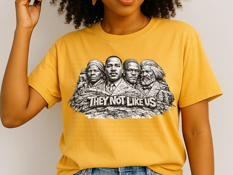 以下が含まれることがあります： マスタードイエローのTシャツ。4人の歴史上の人物が描かれたグラフィックで、マウントラッシュモアに似ており、「THEY NOT LIKE US」の文字が大胆なフォントで書かれています。柔らかい素材で作られています。