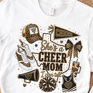 Op de afbeelding: Een wit t-shirt met een grafisch ontwerp van een baseballpet, sneakers, wimpel, strik, megafoon, beker en cheerleading-uniform met luipaardprint. De tekst luidt "She's a CHEER MOM I can tell" over een omtrek van de staat Texas.