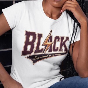 May include: White t-shirt with a brown and gold graphic that says "BLACK" with a lightning bolt and the text "Empowered by my history".