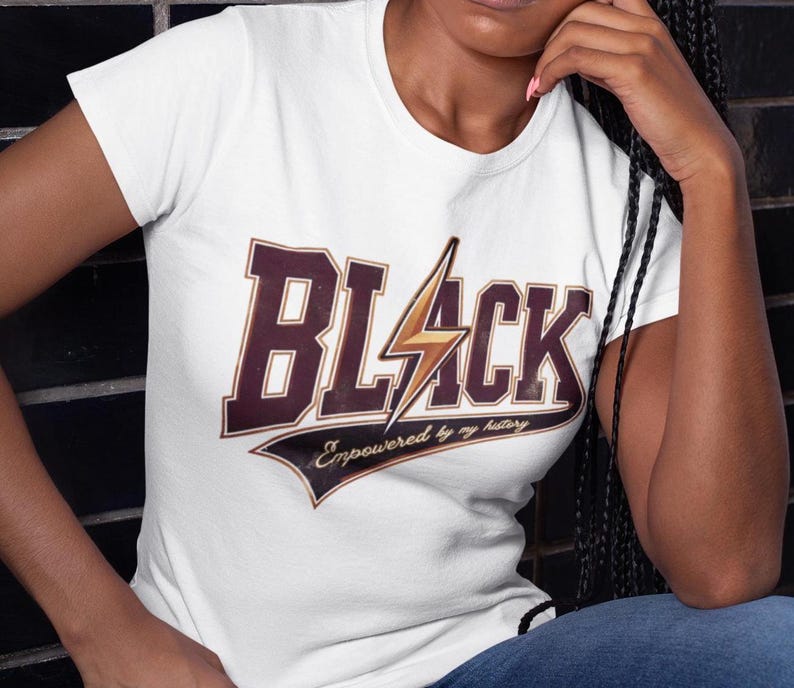 May include: White t-shirt with a brown and gold graphic that says "BLACK" with a lightning bolt and the text "Empowered by my history".