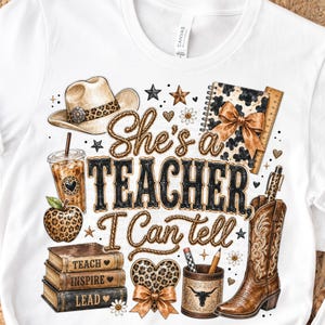 Può includere: Una t-shirt bianca con una stampa grafica che riporta il testo "She's a TEACHER, I Can tell". Il design include un cappello da cowboy, caffè freddo, una mela maculata, una pila di libri, un cuore, un portapenne e uno stivale da cowboy.