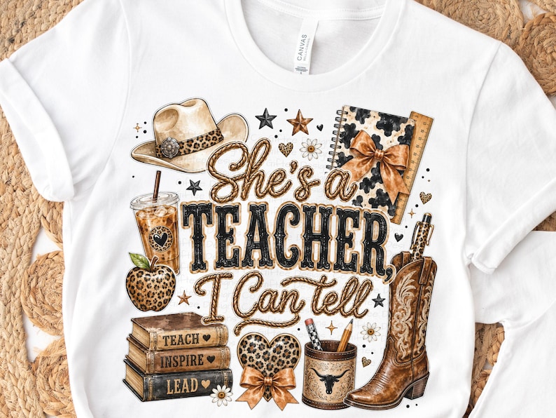 May include: A white t-shirt featuring a graphic print with the text "She's a TEACHER, I Can tell". The design includes a cowboy hat, iced coffee, a leopard print apple, a stack of books, a heart, a pencil holder, and a cowboy boot.