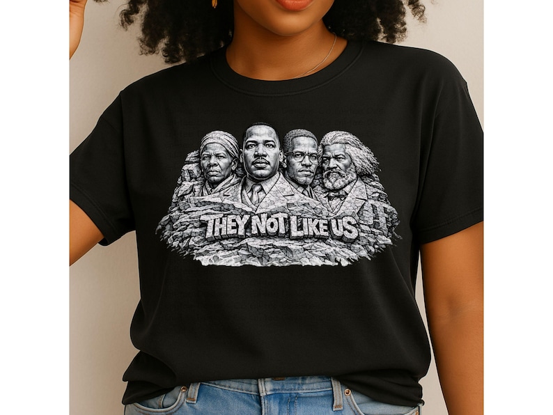 以下が含まれることがあります： 歴史上の人物4人の白黒グラフィックが特徴の黒いTシャツ。記念碑の彫刻に似ています。「THEY NOT LIKE US」の文字が下にあります。柔らかい素材のシャツです。