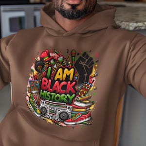 May include: A brown hoodie with a colorful graphic print that says "I AM BLACK HISTORY". The graphic includes a raised fist, musical notes, books, and a boombox.
