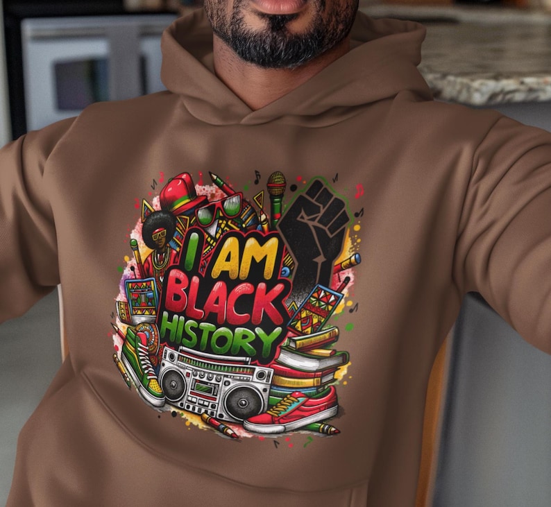May include: A brown hoodie with a colorful graphic print that says "I AM BLACK HISTORY". The graphic includes a raised fist, musical notes, books, and a boombox.
