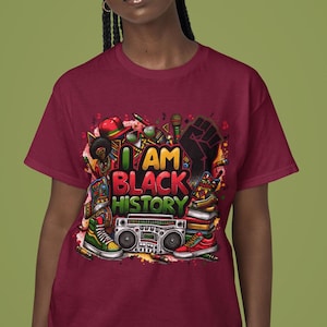 May include: A maroon t-shirt with a colorful graphic design featuring the text "I AM BLACK HISTORY". The design includes a raised fist, books, a boombox, and other objects.
