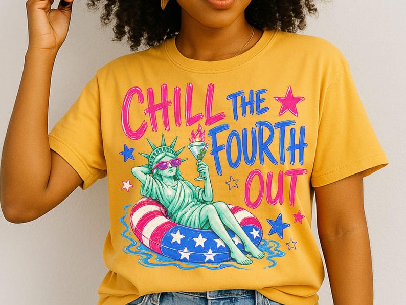 May include: A mustard yellow t-shirt featuring a graphic of the Statue of Liberty wearing pink sunglasses, lounging in a red, white, and blue star-patterned pool float while holding a martini. The text reads CHILL THE FOURTH OUT in pink and blue.