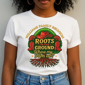 May include: White t-shirt featuring a colorful graphic design. The design includes a red cowboy hat, boots, and the text "Williams Family Reunion, Roots in the Ground, Where my Fam at?" in a circular arrangement around a tree.
