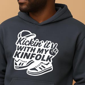 May include: Dark navy blue hoodie with a white graphic that says "Kickin' it with my Kinfolk". The graphic includes a baseball cap, sneakers, and a peace sign. The hoodie has a hood and a front pocket.