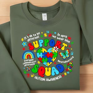 May include: Green sweatshirt with a colorful graphic design that says "Support Squad" and "Autism Awareness". The graphic includes a rainbow, a heart made of puzzle pieces, a butterfly, and other symbols.