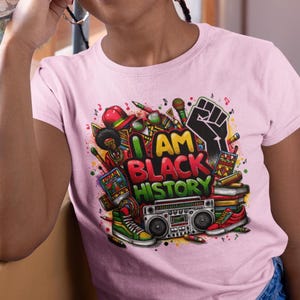 May include: Pink t-shirt with a colorful graphic design featuring a fist, musical notes, and the text "I AM BLACK HISTORY".