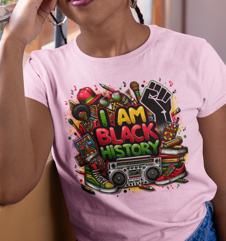 May include: Pink t-shirt with a colorful graphic design featuring a fist, musical notes, and the text "I AM BLACK HISTORY".